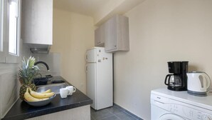 A compact kitchen with a refrigerator, a washing machine, a coffee maker, and a bowl of fruit. - Ano Patisia A Fully Renovated Penthouse (Athens)