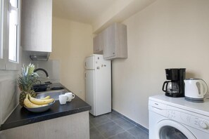 A compact kitchen with a refrigerator, a washing machine, a coffee maker, and a bowl of fruit. - Ano Patisia A Fully Renovated Penthouse (Athens)