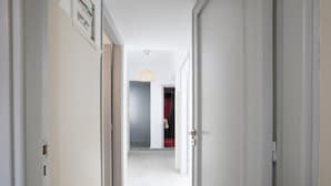 A hallway with white walls and doors, leading to a room with a red door and a hanging light fixture. - Ano Patisia A Fully Renovated Penthouse (Athens)