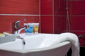 A bathroom with a white sink, red tiled walls, and a shower area. - Ano Patisia A Fully Renovated Penthouse (Athens)