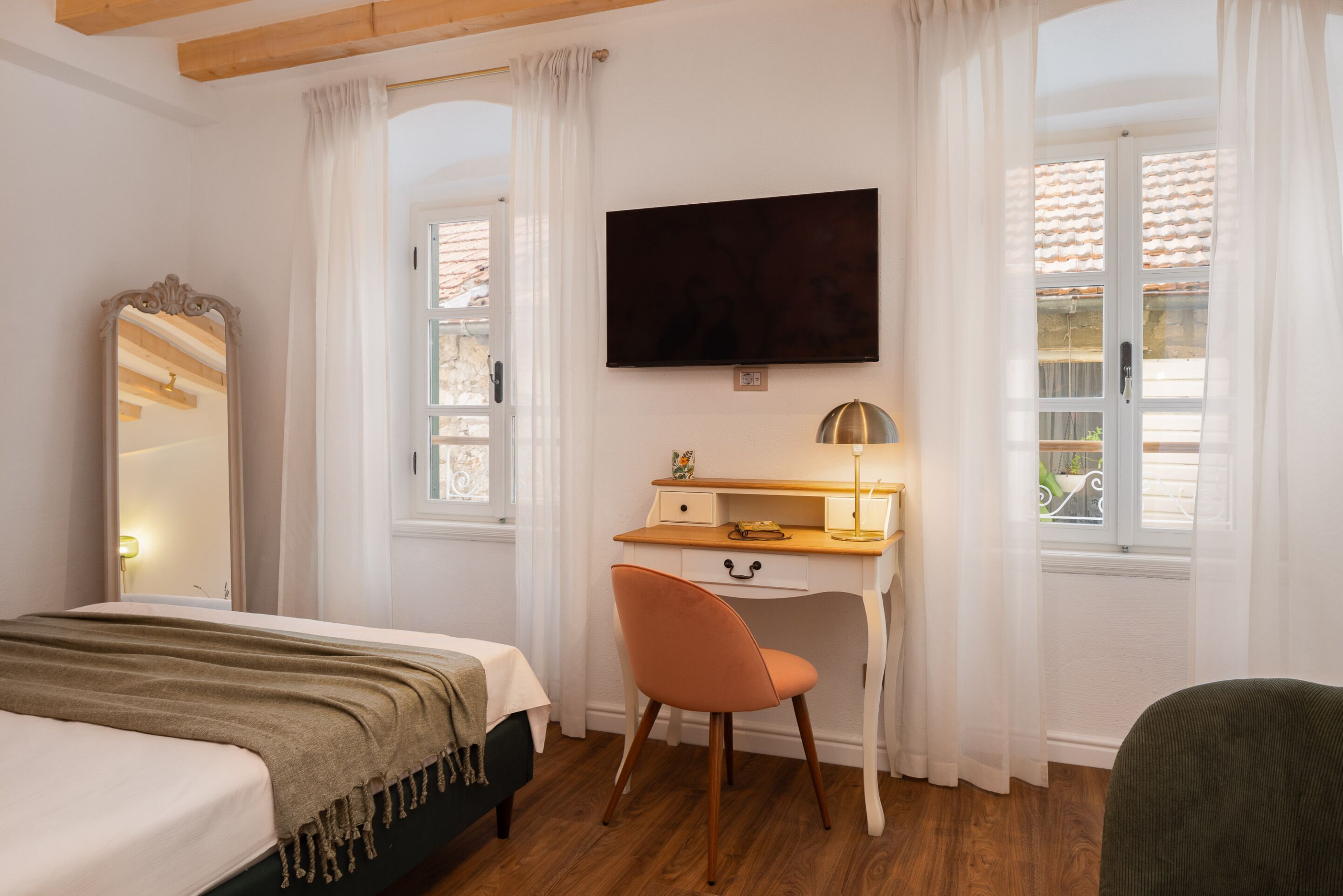 A bedroom with a bed, a desk, a chair, a television, and a window with curtains.