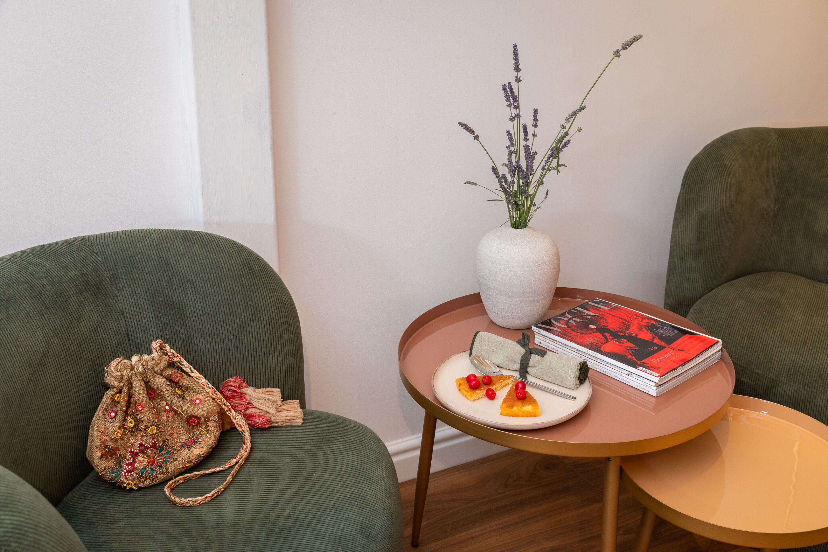 A room with a green sofa, a small round table with a vase of flowers, a book, and a decorative bag.