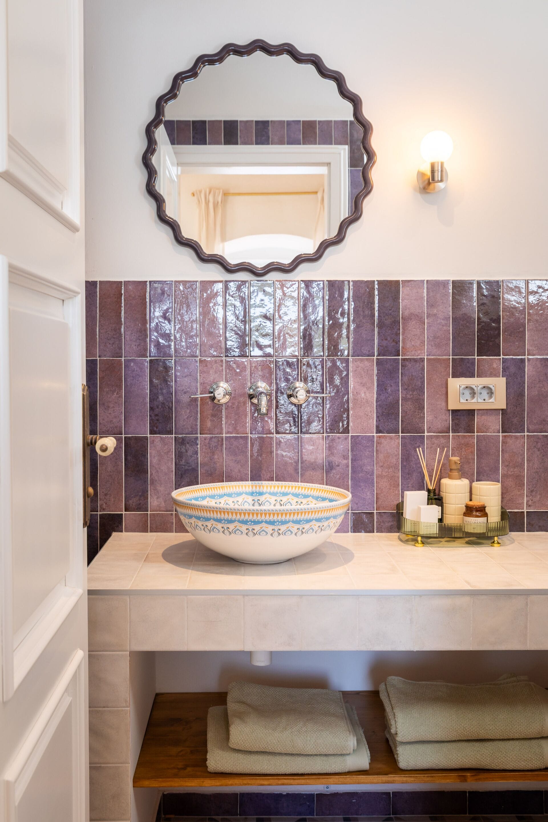 Un baño con un lavabo ovalado grande, un espejo montado en la pared, una lámpara y un salpicadero de azulejos.