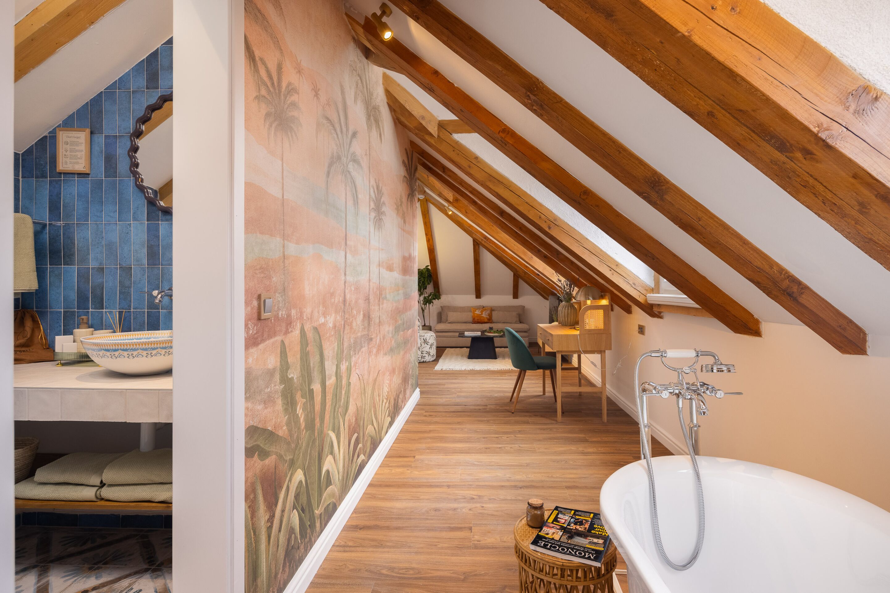 A modern bathroom with a freestanding bathtub, wooden beams, and a tiled wall with a mural.