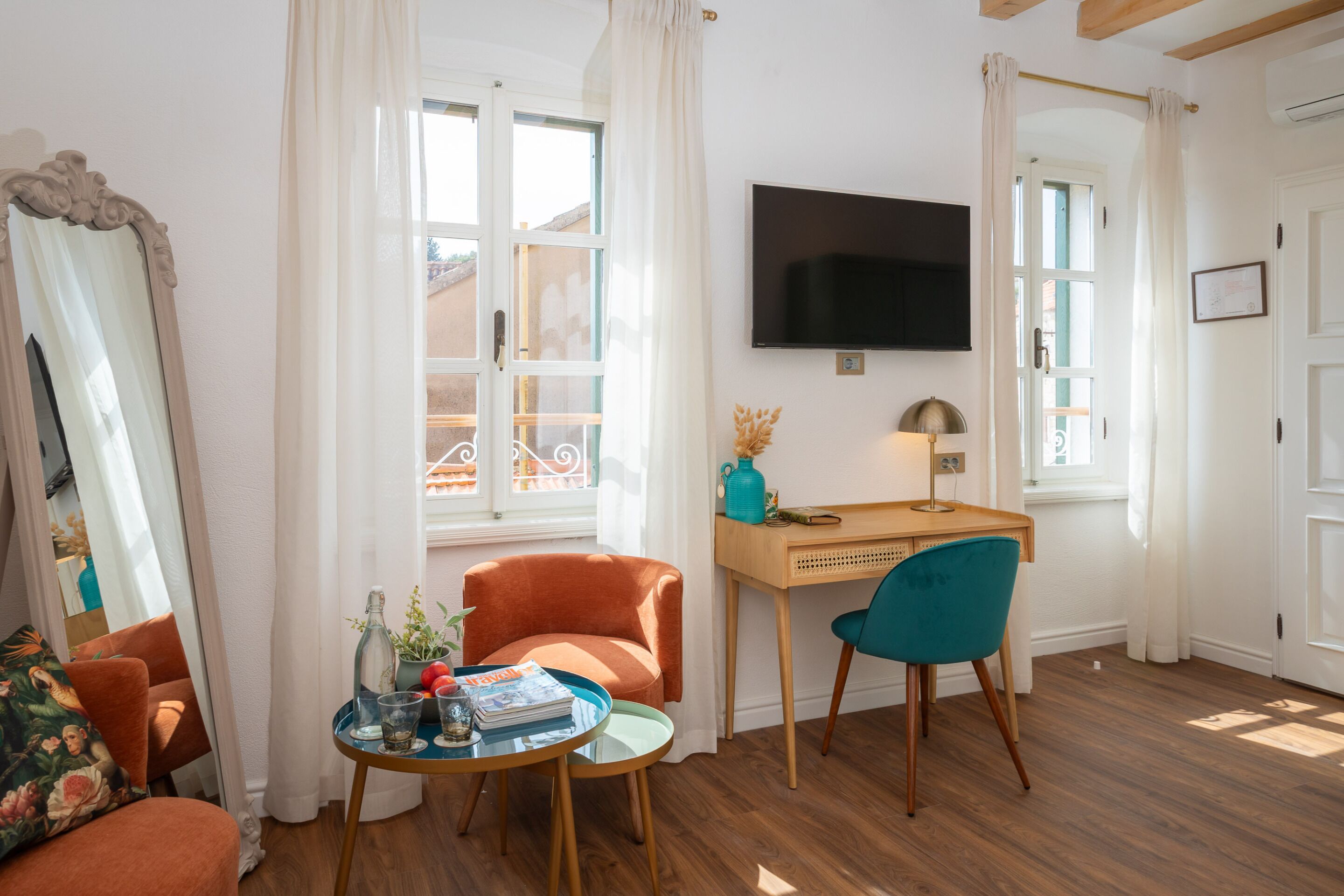 Une pièce avec un bureau en bois, une télévision, un canapé et une fenêtre avec des rideaux.