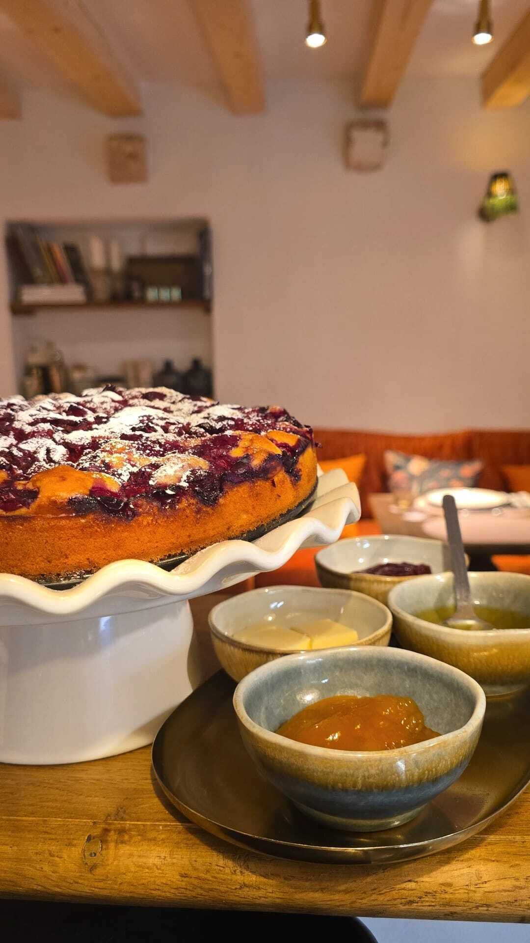 Un dessert servi dans un plat blanc, accompagné de trois petits ramequins contenant des sauces, le tout présenté sur une table en bois dans un restaurant.