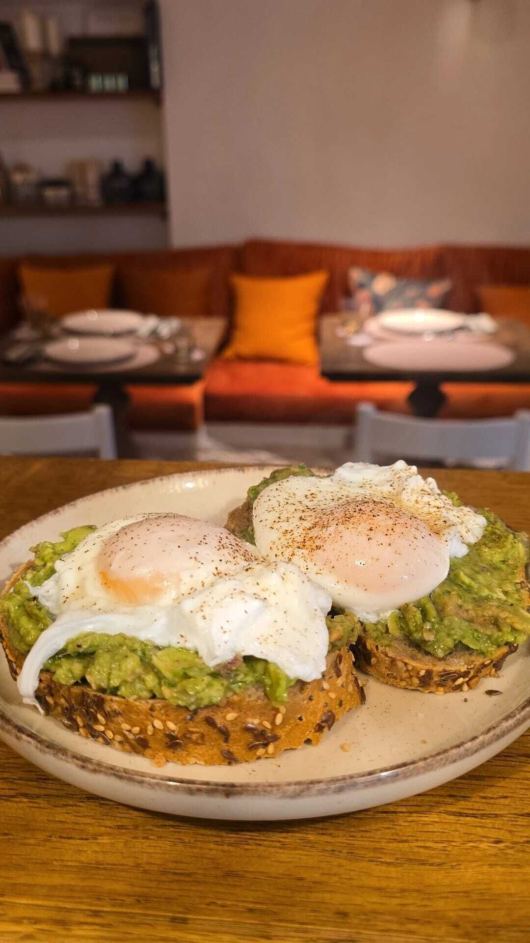 A plate of avocado toast with poached eggs on a wooden table.