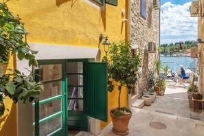 A narrow street with a yellow building, a green door, and a potted plant.