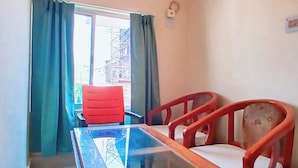 A room with a glass-top table, two red chairs, a TV mounted on the wall, and an air conditioning unit. - Moon View Homestay (Guwahati)