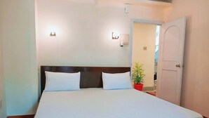 A bed with white linens, a wooden headboard, two wall-mounted lights, and a potted plant. - Moon View Homestay (Guwahati)