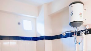 A bathroom with white tiles, a blue accent strip, a toilet, a sink, and a shower with a water heater. - Moon View Homestay (Guwahati)