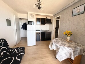 Un espace de vie compact comprenant un coin cuisine, un coin repas avec une nappe à motifs et un tableau accroché au mur.