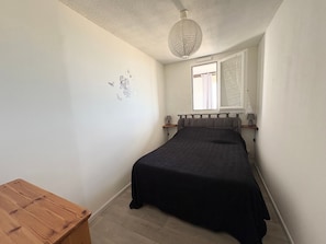 Une chambre à coucher avec un lit, une table en bois, un luminaire suspendu et une fenêtre avec des rideaux.