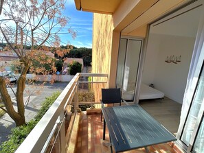 A balcony with a table and chairs, a sliding glass door, and a view of the street and trees. - Convenient apartment for 2 guests near the beach (Argelès-sur-Mer)