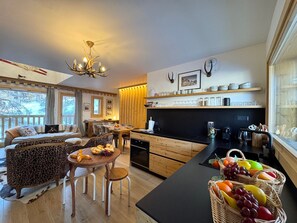 A cozy living room with a sofa, a dining table, and a kitchen area with a counter and fruit baskets. - Spacious chalet in Vars for 12 ppl (Vars)