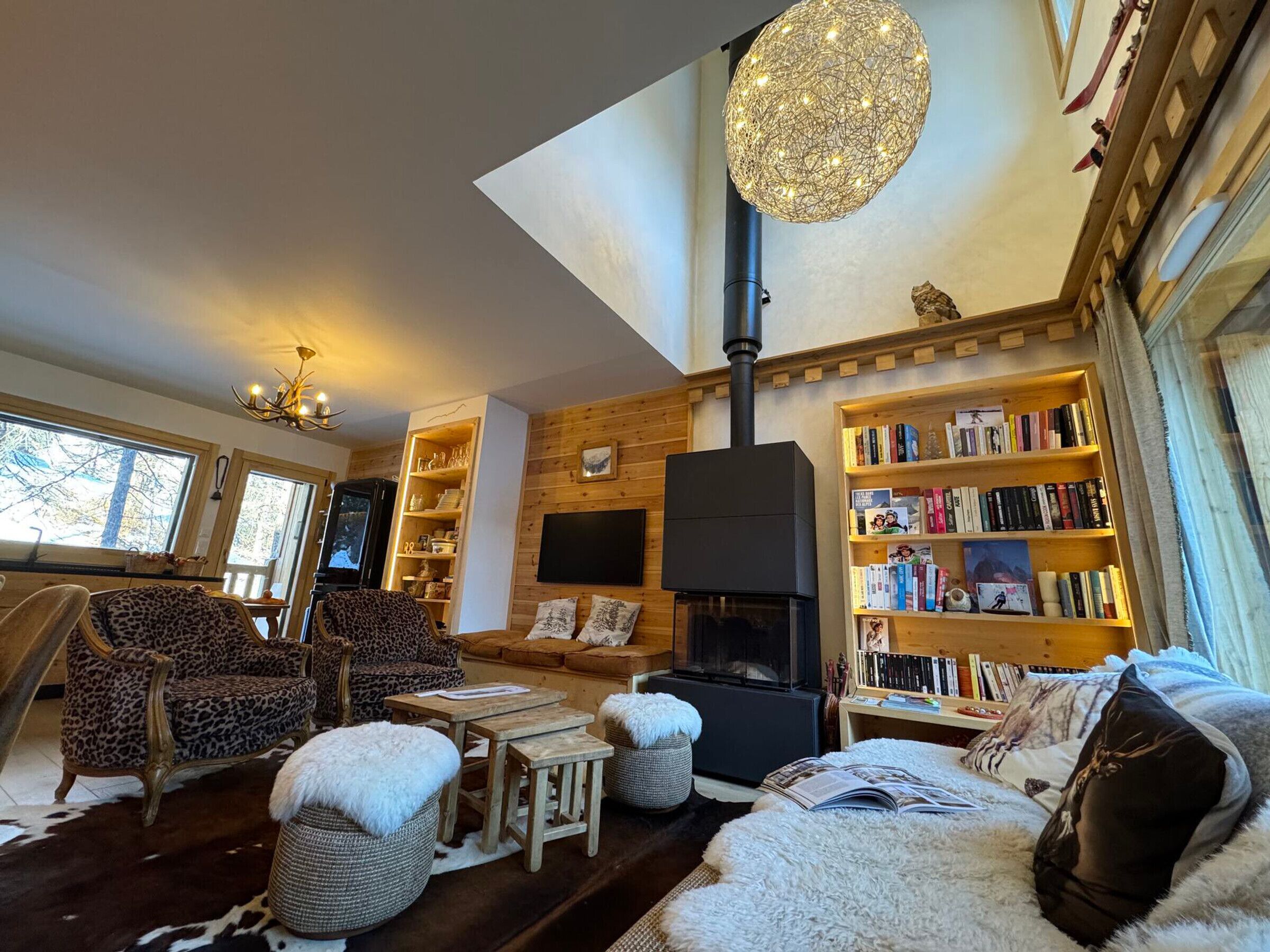 A cozy living room with a fireplace, bookshelves, and a large window.
