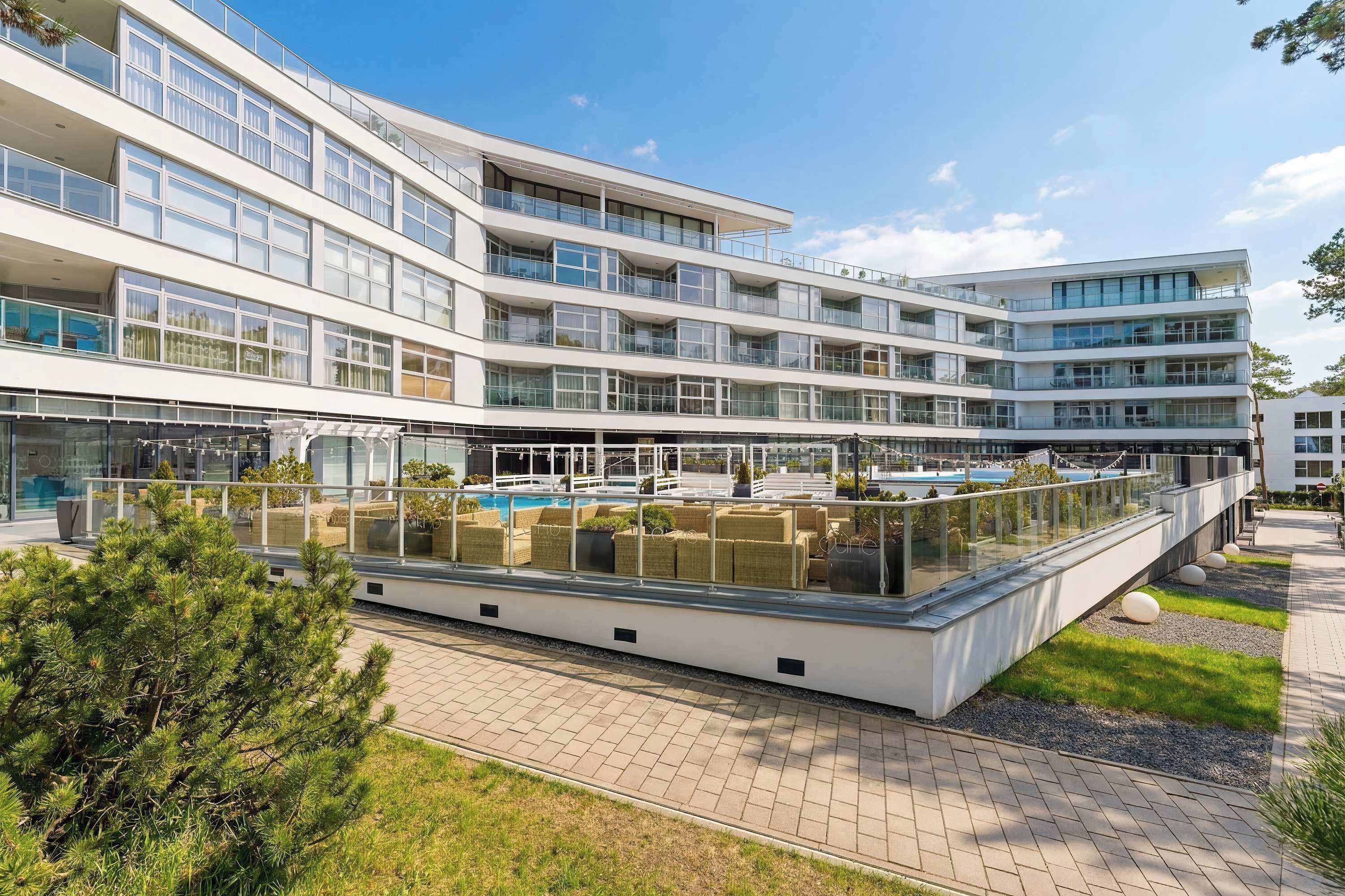 A multi-story hotel with a rooftop pool area, outdoor seating, and a well-maintained garden.