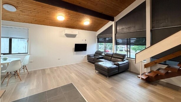 Uma sala de estar moderna com teto de madeira, uma TV de tela plana, um sofá cinza e uma escada.