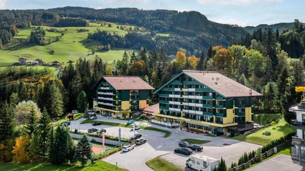 Un hotel con un corpo centrale e due ali, circondato da un parcheggio e aree verdi.