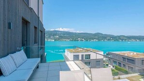 Um edifício moderno com terraço no telhado, vista para um corpo de água e montanhas ao longe.