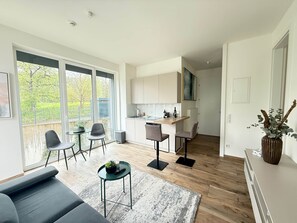 A modern living room with a sofa, a coffee table, and a dining area with chairs. - Hermitage Apartment A09 - Lake view & access (Maria Wörth)