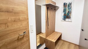 Una habitación con puerta de madera, pared blanca, banco de madera, tubería negra y un cuadro.