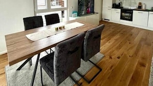 Una cocina moderna con armarios blancos, una zona de comedor con mesa y sillas de madera, y un ventanal con vistas a la vegetación.