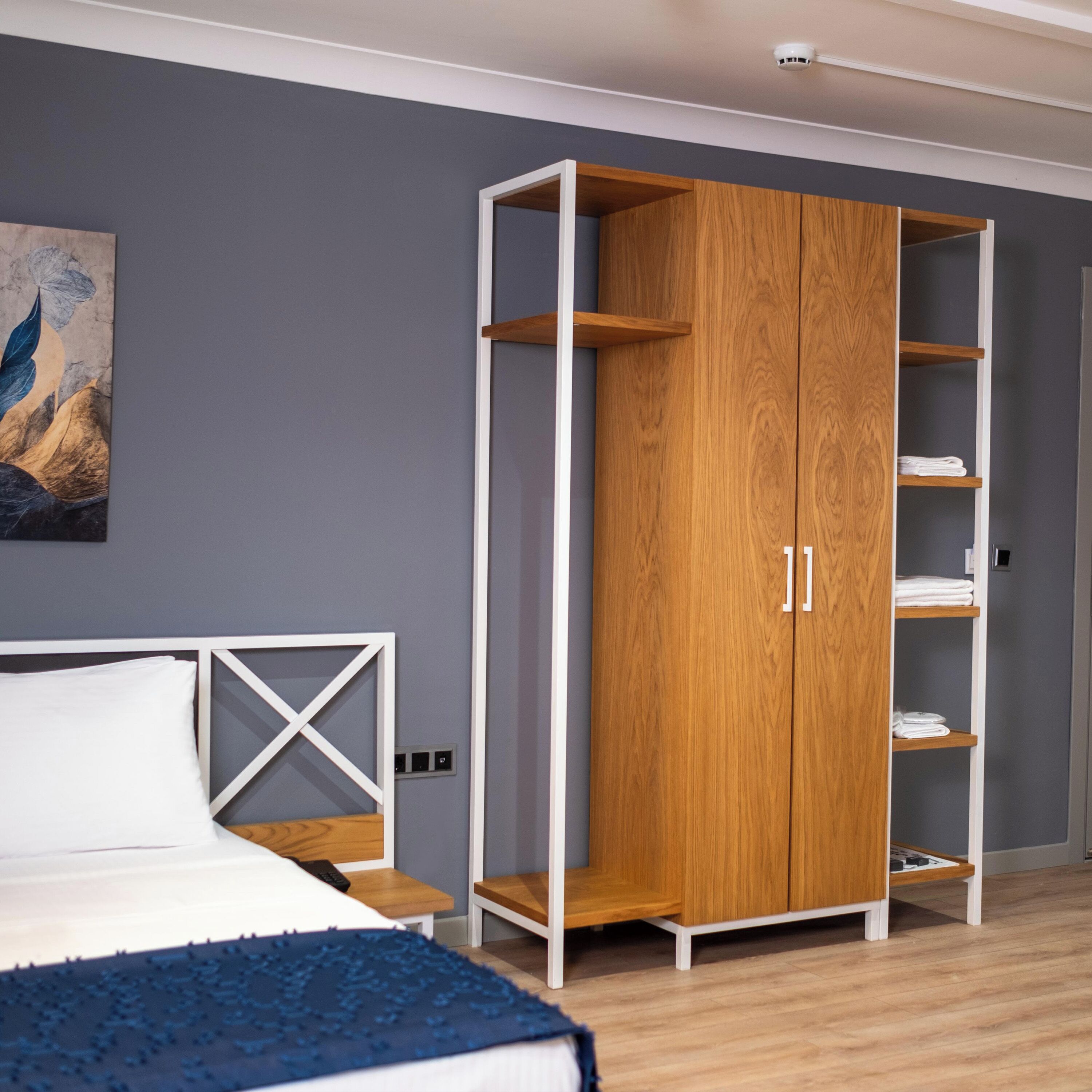 A bedroom with a bed, a wooden wardrobe with shelves, and a painting on the wall.