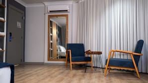 A room with a wooden floor, two blue armchairs, a small table, a mirror, and a door with an air conditioning unit. - Mec Avila (Amasya)