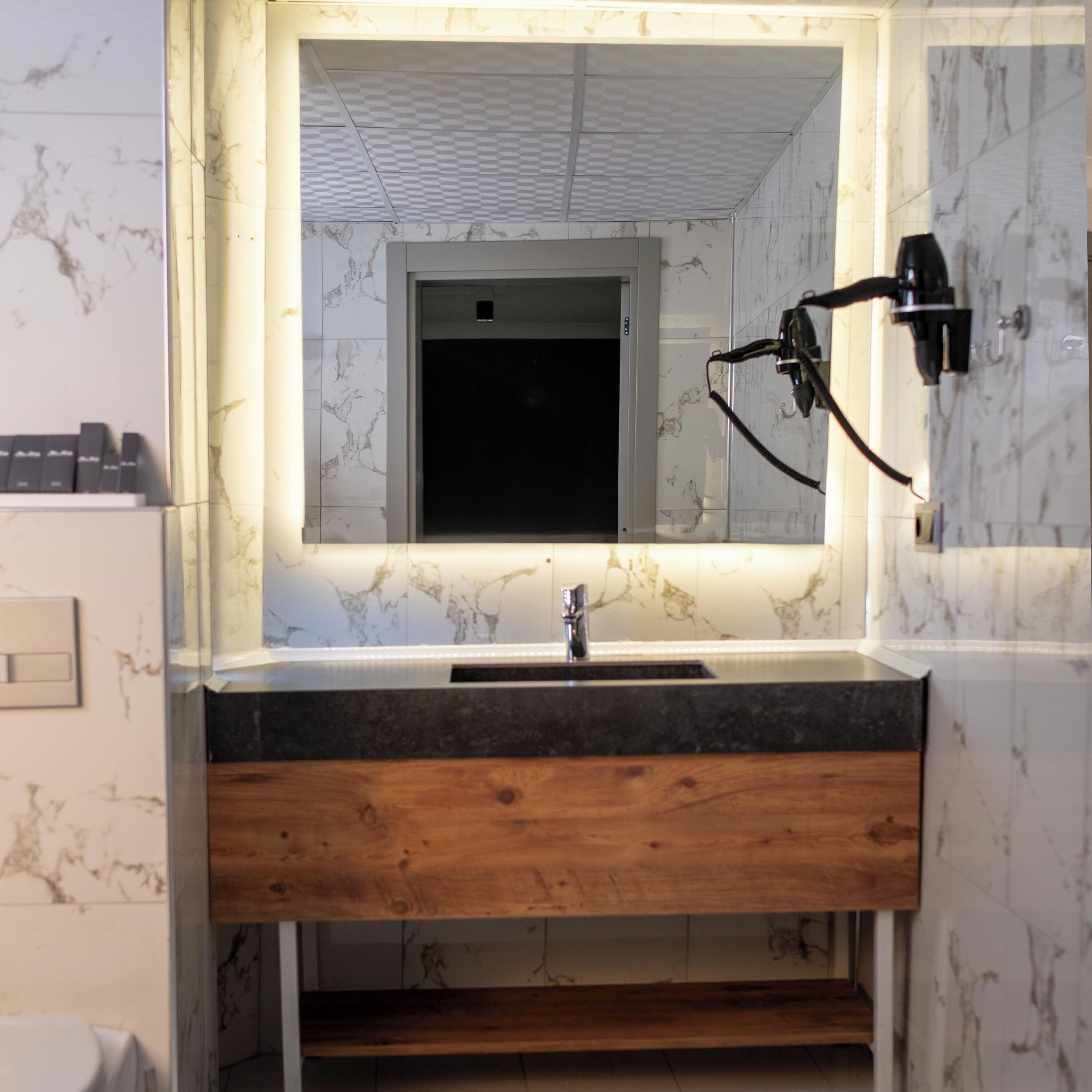A bathroom with a marble wall, a wooden vanity, a sink, and a mirror.