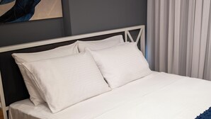 A bed with white bedding, a wooden nightstand, and a blue blanket. - Mec Avila (Amasya)