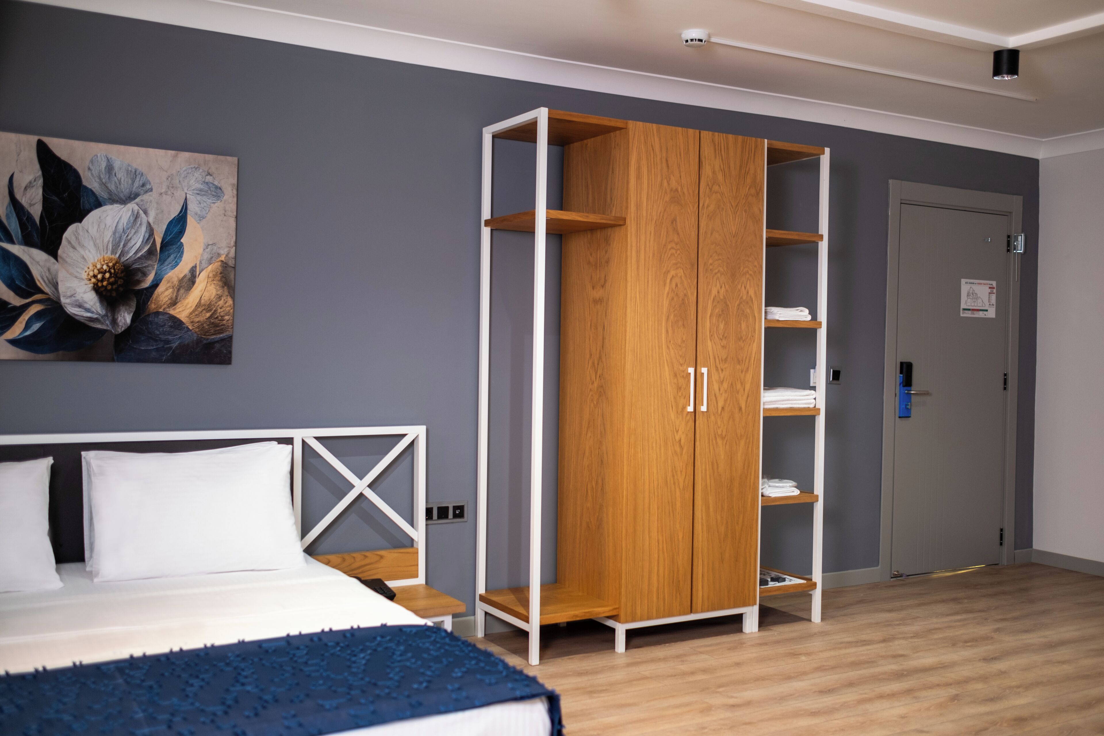 A bedroom with a bed, a wooden wardrobe, a painting, and a door.