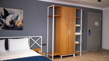 A bedroom with a bed, a wooden wardrobe, a painting, and a door.