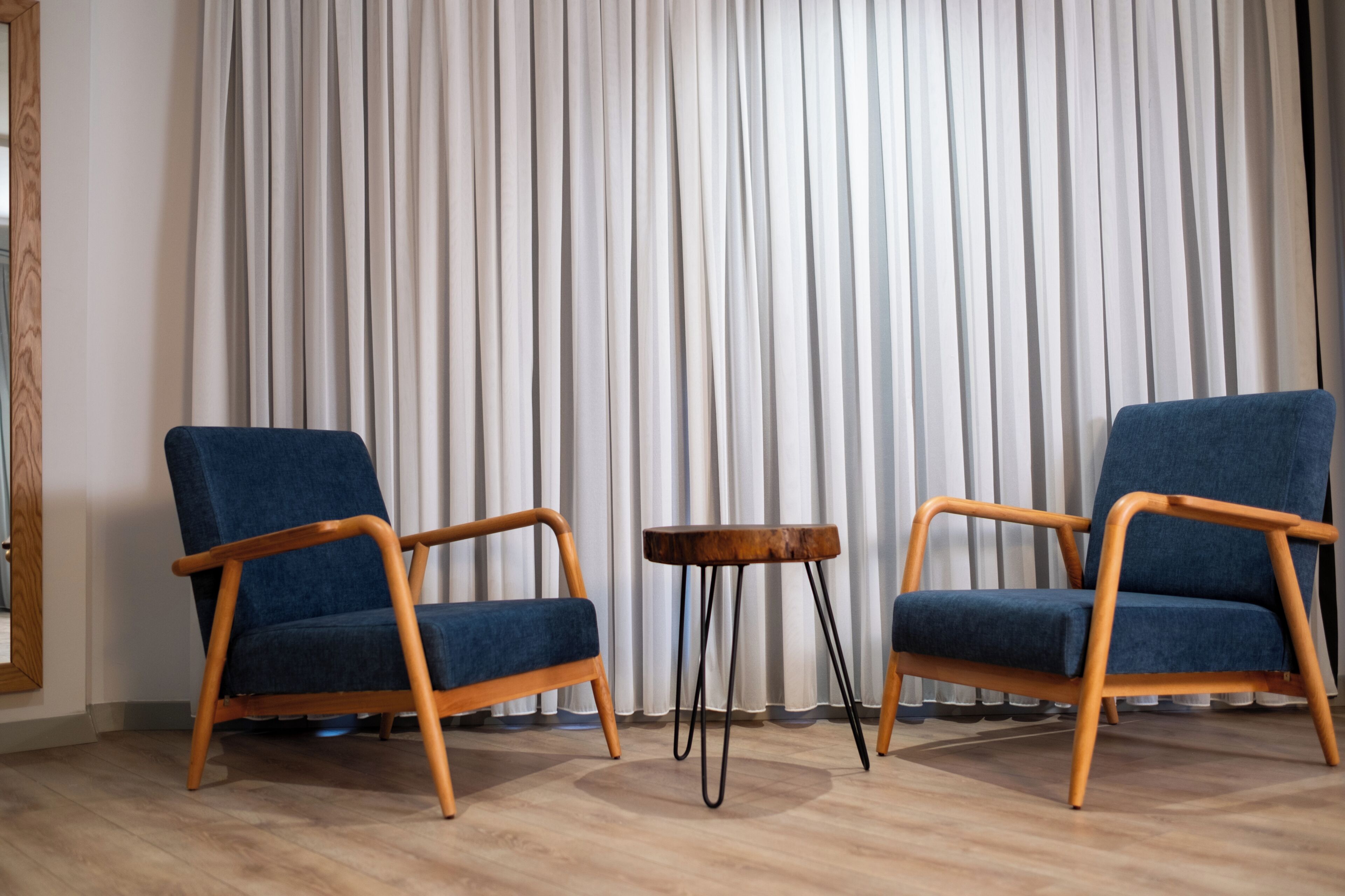 Dos sillones azules con estructura de madera, una mesita de madera y un telón de fondo.