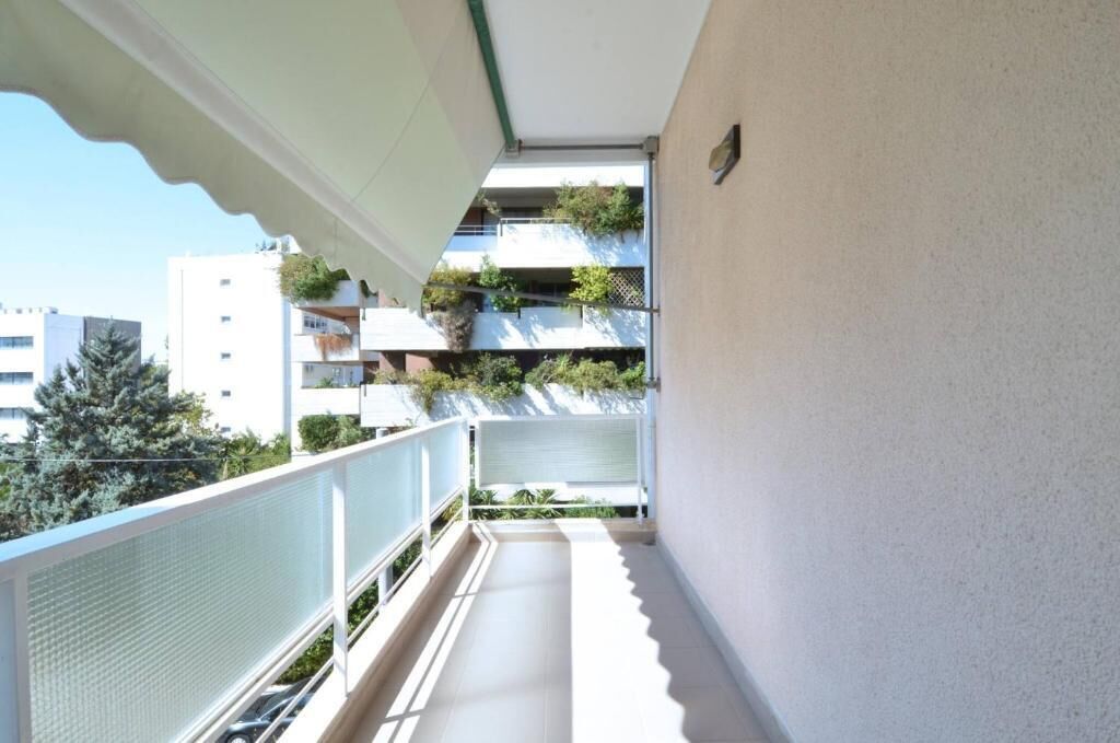 A narrow balcony with a white railing, a view of adjacent buildings, and a clear sky.