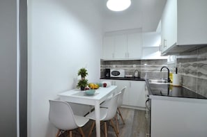 A compact kitchen with white cabinets, a microwave, and a sink. There is a dining table with chairs and a bowl of fruit. - Spacious minimal apartment at Chalandri (Chalandri)