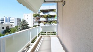Ein Balkon mit weißer Reling, Kachelboden und Blick auf angrenzende Gebäude.