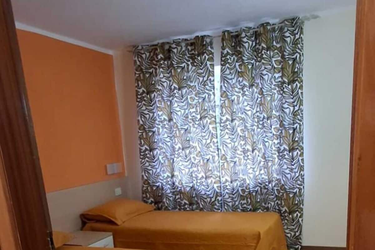 Una habitación con tres camas, una cortina estampada y un suelo de tonos claros.