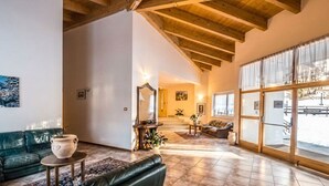 Un vaste espace de vie doté d’un plafond en bois, d’un canapé vert, d’une table basse et d’une grande fenêtre donnant sur l’extérieur.