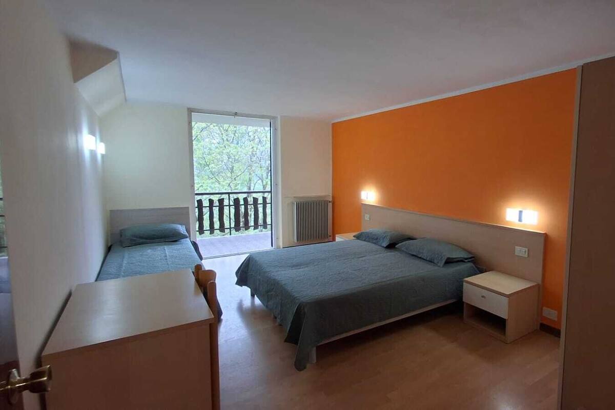 Un dormitorio con cama, mesitas de noche, un escritorio y un balcón.