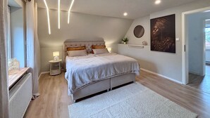 A bedroom with a bed, bedside tables, a radiator, a wall-mounted artwork, and a door leading to another room. - Holiday Home 'Kokorey' with Private Terrace, Garden and Wi-Fi (Rellingen)