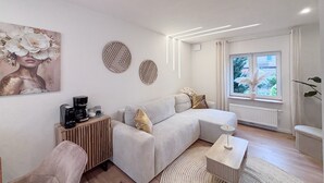 A modern living room with a sofa, a coffee table, a side table, and decorative wall art. - Holiday Home 'Kokorey' with Private Terrace, Garden and Wi-Fi (Rellingen)