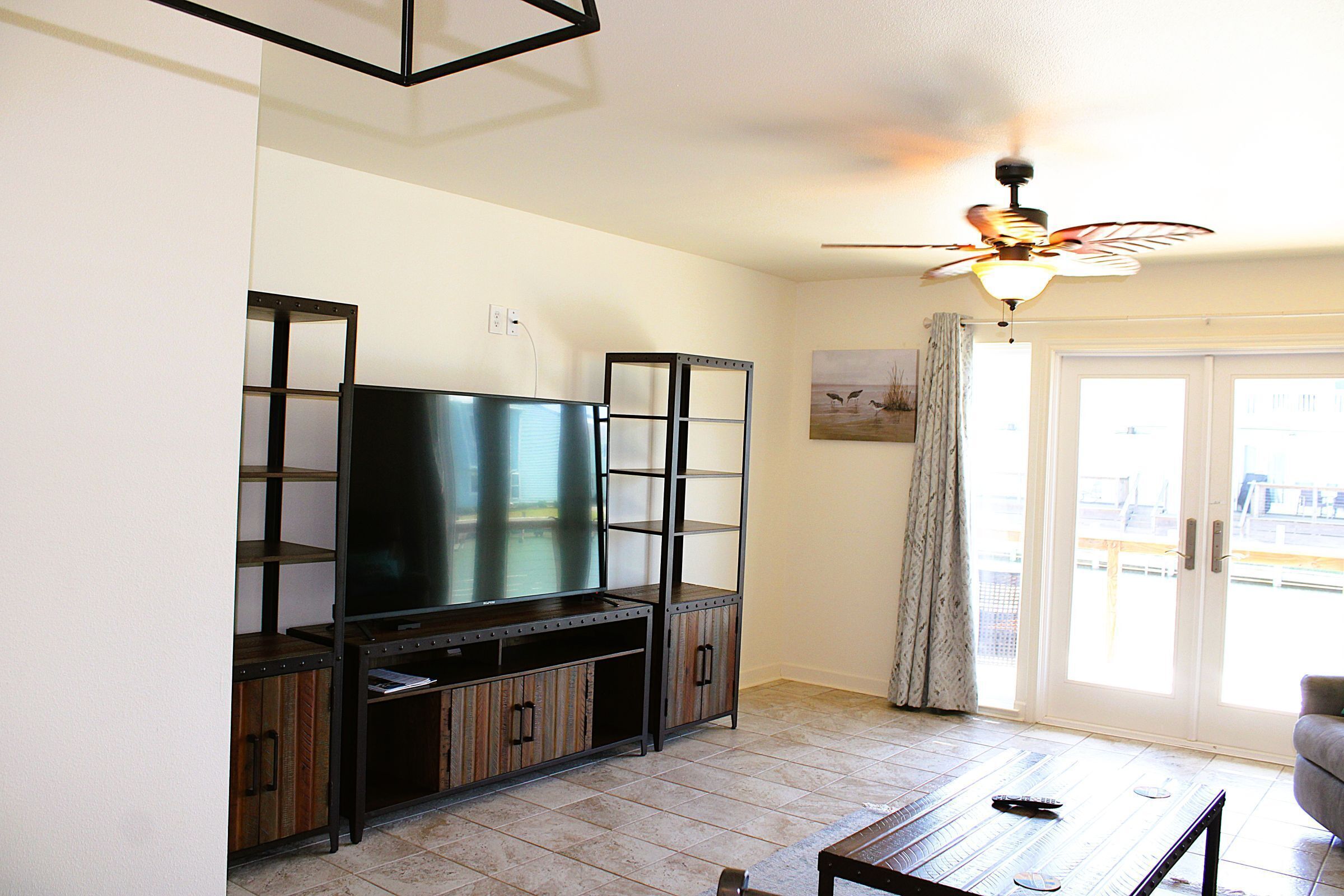 A living room with a flat-screen TV, wooden cabinets, a ceiling fan, and a sliding glass door.