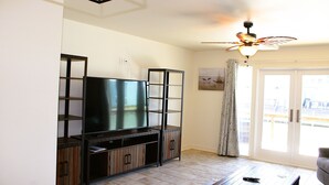 Ein Wohnzimmer mit Flachbildfernseher, Holzkredänzen, Deckenventilator und einer Schiebetür aus Glas.