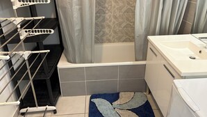 Un baño con bañera, cortina de ducha, lavamanos y toallero.