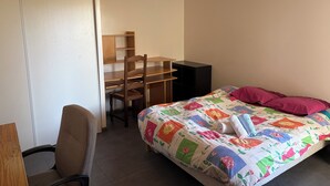 Un dormitorio con una cama, un escritorio con silla y un armario.