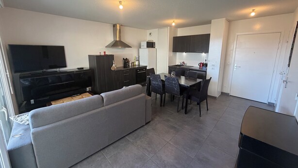 Una sala de estar moderna con sofá, televisión y comedor con sillas y mesa.