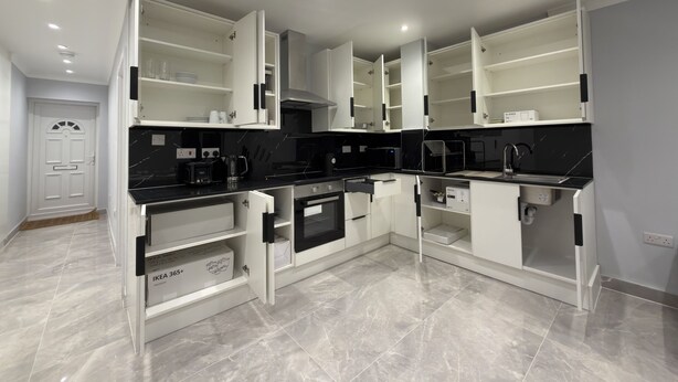A modern kitchen with white cabinetry, black countertops, and a tiled floor.