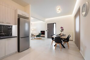 A modern kitchen with a built-in refrigerator, dining area with a table and chairs, and a TV in the background.