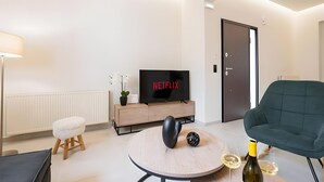 A modern living room with a television, a round coffee table, a green armchair, and a bottle of wine. - Apartment 'Zoelgrek Luxury Suite 1' with Private Terrace, Wi-Fi and Air Conditioning (Iraklio)